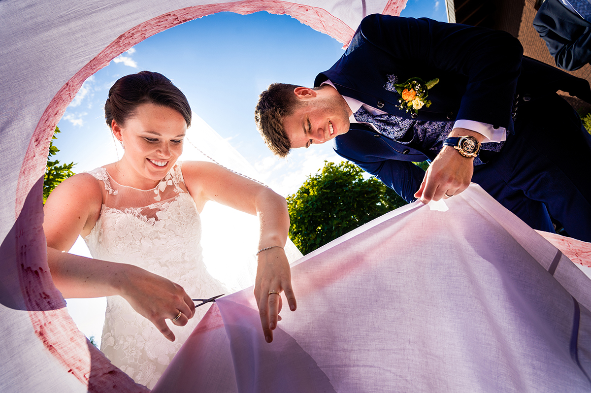 Bride and groom cutting a sheet together as part of a wedding tradition in northern Germany by Potok's World Photography